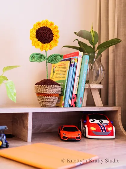 The potted sunflower sitting amongst books and toy cars on a child's desk. It's a versatile piece of decor that fits in perfectly with a playful environment.