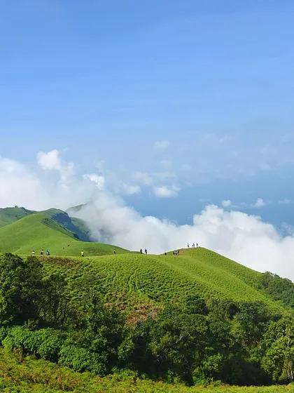 A stunning landscape view of the green meadows of Bandaje, with trekkers scattered across the hills.