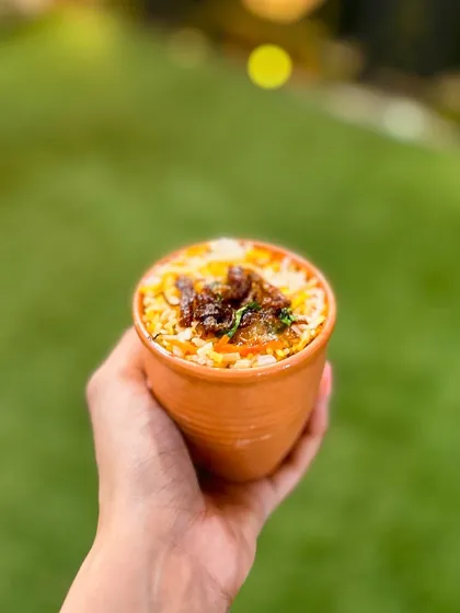 My Kulhad Biryani is served in individual clay pots for an earthy, rustic flavour. This image shows a hand holding up a kulhad, highlighting the personal and traditional serving style.