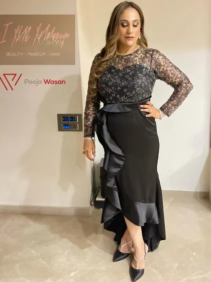 A full-length view of a chic and elegant party look. The client wears a modern black dress, and her makeup is kept sophisticated with soft smokey eyes and highlighted curls.