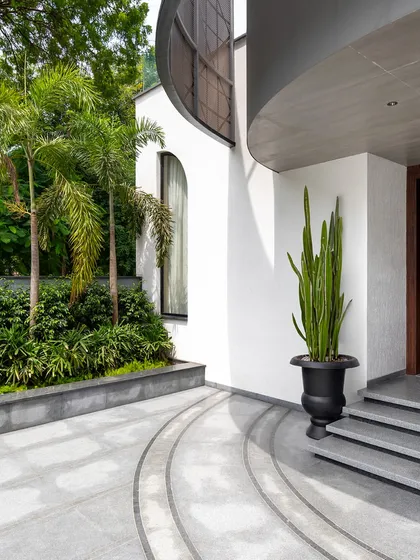 The curved entrance of the Juneja Residence, framed by lush palm trees and minimalist landscaping. We use organic forms and natural elements to soften modern architecture and create a harmonious entry sequence.