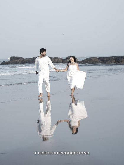 A stunning reflection shot of a couple holding hands and walking on a wet beach in Goa, creating a beautiful, symmetrical image.