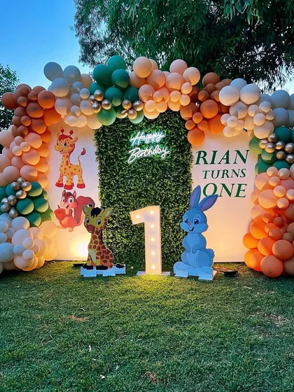 We created this beautiful outdoor jungle theme for Rian's first birthday, using a faux-grass wall as a natural backdrop for our balloon arch, marquee number, and cute animal cutouts.