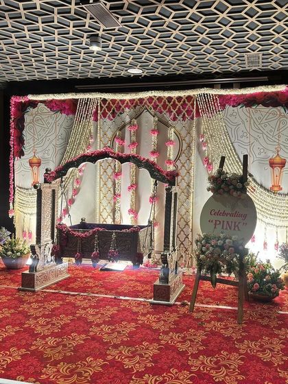A lovely naming ceremony setup with a wooden cradle decorated in pink flowers, set against a floral backdrop.