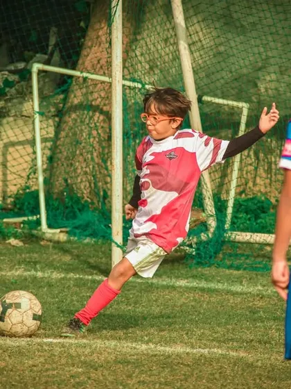 A young player with glasses takes a shot on goal.