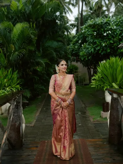 A full-length portrait of the South Indian bride, walking on a path surrounded by lush greenery. Her grace and beautiful attire are the focus.