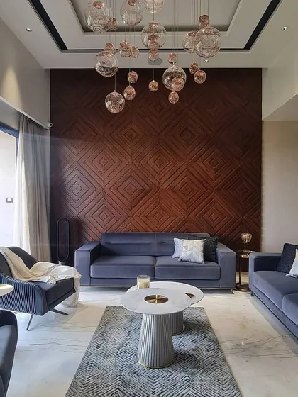 In this living room, we created a feature wall with an intricate geometric pattern in dark wood, adding warmth and texture to the space. The design is complemented by modern blue sofas, marble coffee tables, and a cluster of glass globe pendant lights.
