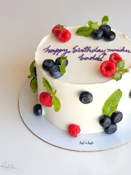 A simple yet beautiful celebration cake with chocolate buttercream, decorated with fresh raspberries, blueberries, and mint leaves for a pop of color and flavor.