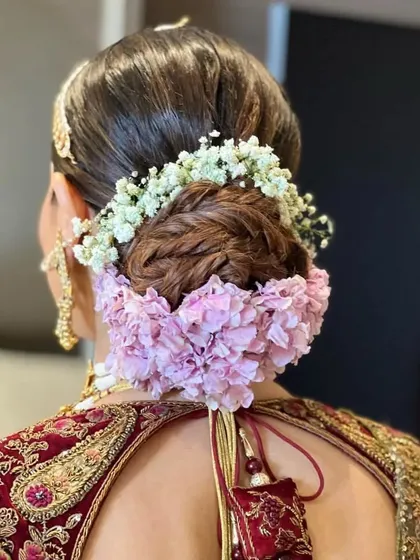 A back view of a braided bun adorned with a combination of baby's breath and pink hydrangeas. The texture and colors create a beautiful and romantic bridal updo.