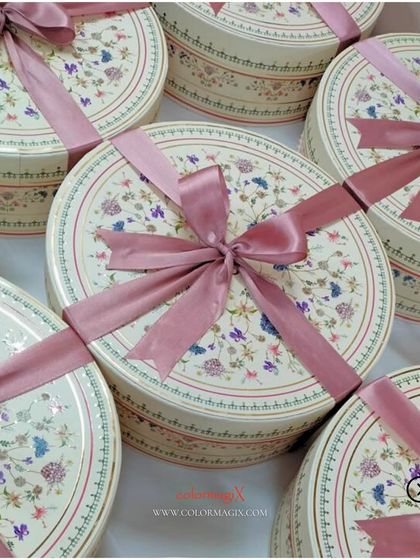 A collection of our round floral wedding favor boxes, tied with beautiful pink satin ribbons, ready for a wedding celebration.