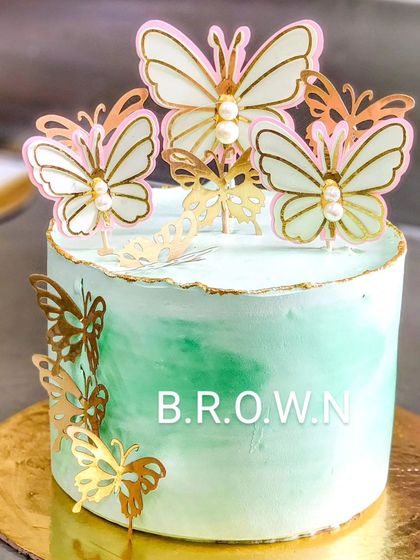 A customized butterfly theme cake with a green marble effect. The cake is adorned with delicate gold and white butterflies, creating a simple yet stunning design.