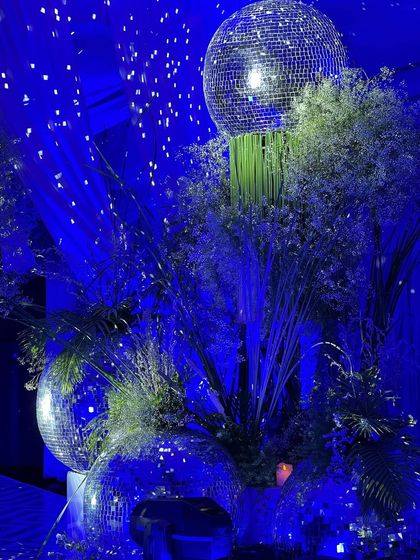 Another centerpiece detail, showing multiple disco balls of varying sizes integrated into a lush floral and foliage arrangement. The deep blue lighting makes the entire installation sparkle.