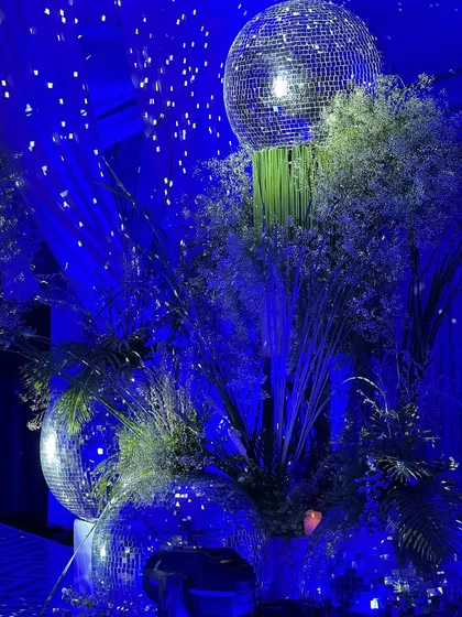 Another centerpiece detail, showing multiple disco balls of varying sizes integrated into a lush floral and foliage arrangement. The deep blue lighting makes the entire installation sparkle.