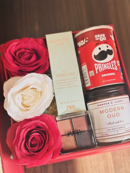 A Valentine's Day hamper for the beauty lover, including a Zara perfume, a Nykaa eyeshadow palette, a "Modern Oud" candle, and Pringles for a fun snack.