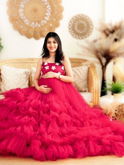 A radiant mom-to-be in a bright pink ruffled gown, seated comfortably in our sunny boho studio.