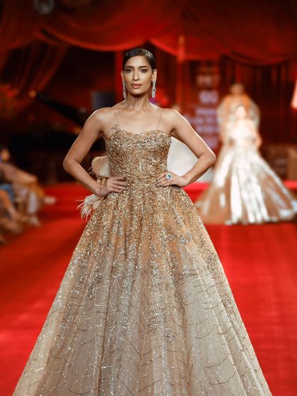 A model strikes a pose in a magnificent golden ball gown. This is a classic couture shot, emphasizing the grandeur and craftsmanship of the dress.