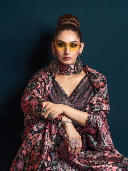 A bold studio portrait of Ragini Dwivedi for a magazine feature. The styling with yellow-tinted glasses and heavy jewelry creates a unique, high-fashion statement.