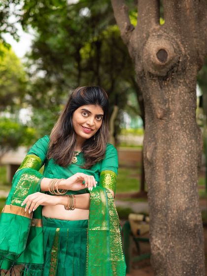 A smiling portrait in a green traditional outfit, taken against a natural tree backdrop. This shot feels both posed and natural.
