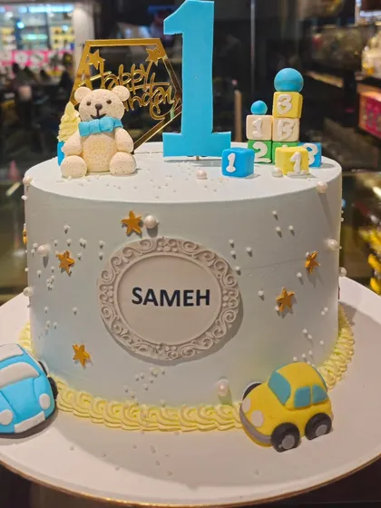 A sweet and classic first birthday cake for a little boy. This cake is decorated with fondant teddy bears, toy cars, and building blocks, capturing the joy of turning one.