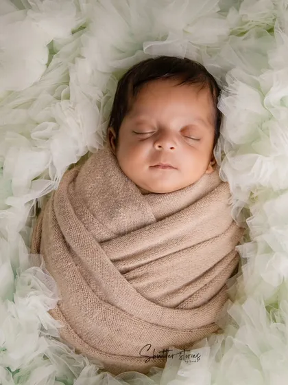 A simple and elegant portrait using a neutral wrap against a soft, textured green background. This highlights the baby's peaceful features.