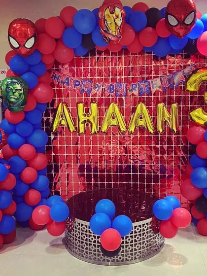 A superhero-themed decoration for a third birthday, using a red shimmer backdrop and balloon arrangements with Spiderman and Iron Man foil balloons.