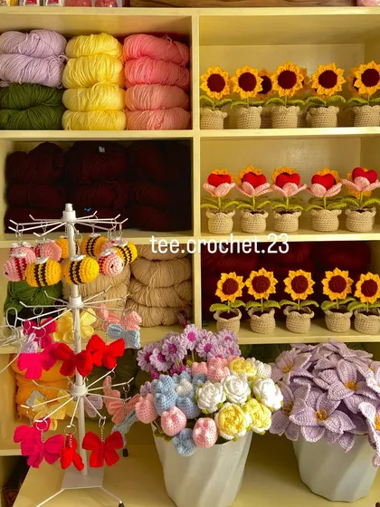 My workshop corner, showing yarn, amigurumi bees, and rows of potted sunflowers and heart flowers.