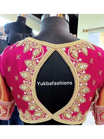 A keyhole back design on a vibrant pink blouse. The opening is framed with intricate gold zardosi leaf patterns, creating an elegant and eye-catching detail for a bridal look.