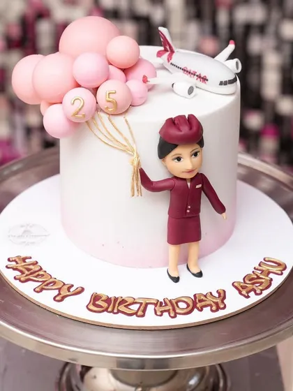 A chic and simple cake for a 25th birthday, themed around a flight attendant's career. The design features a figurine in uniform, an airplane, and pink balloons.