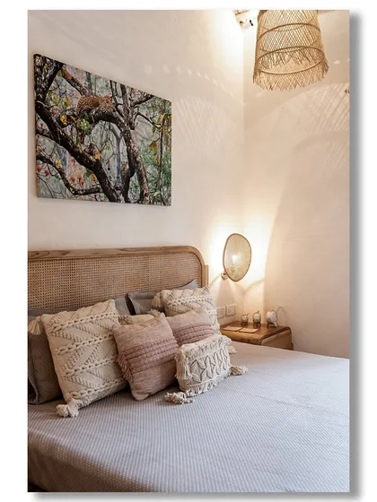 A serene bedroom in a Goan villa, with a rattan headboard, macrame cushions, and a woven lampshade that casts beautiful shadows. The space is a perfect example of relaxed, bohemian luxury.