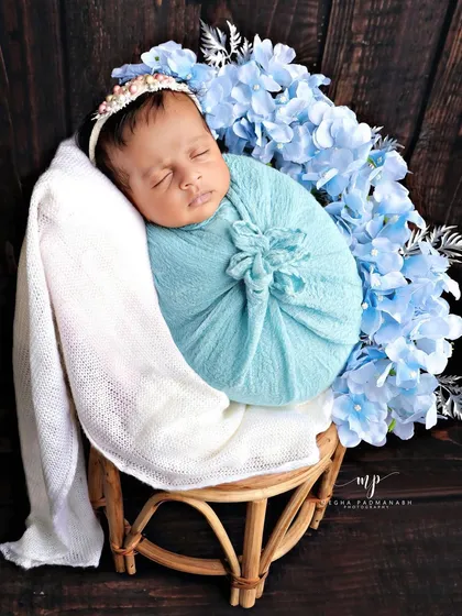 This portrait highlights our use of color and texture. The baby is wrapped in a soft blue swaddle, posed on a miniature rattan chair against a dark wood background, creating a beautiful, high-contrast image.