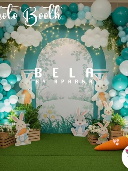 This photo booth is designed with a soft, illustrated backdrop and a floor of artificial grass. The space is filled with cute rabbit cutouts and a giant carrot prop, creating a perfect spot for charming birthday photos.