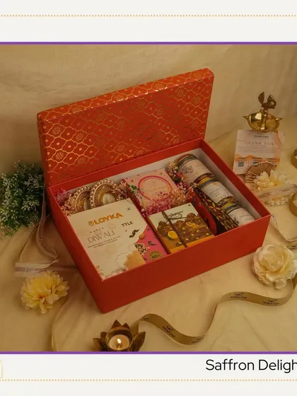 The 'Saffron Delight' hamper. A vibrant orange box filled with festive essentials like almond brittle, honey twigs, and decorative diyas, perfect for spreading Diwali cheer.