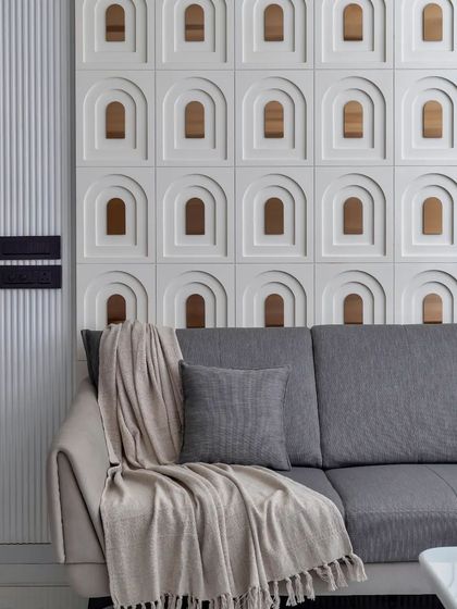 The living room of 'The White Abode' features a stunning feature wall of custom 3D tiles with arched niches and metallic inserts, creating a play of light and shadow.