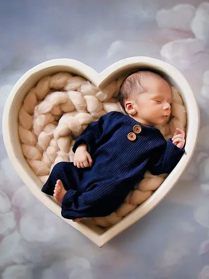 A sweet baby boy in a blue outfit rests inside a heart-shaped bowl against a dreamy, cloud-like background. This simple yet powerful setup is all about love.