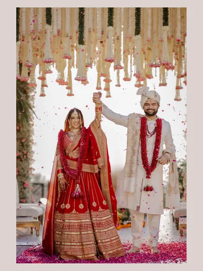 A joyous portrait of the couple, with the intricate floral ceiling of the mandap visible above them. The shower of rose petals adds to the celebratory atmosphere.