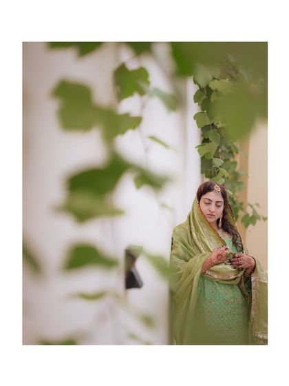 An artistic portrait of a Kashmiri bride, framed by green leaves, her expression serene and graceful.