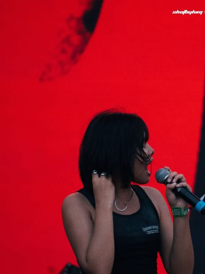 A profile shot of Kim the Beloved against a stark red background at Rolling Loud India. The simple, powerful composition emphasizes her presence.