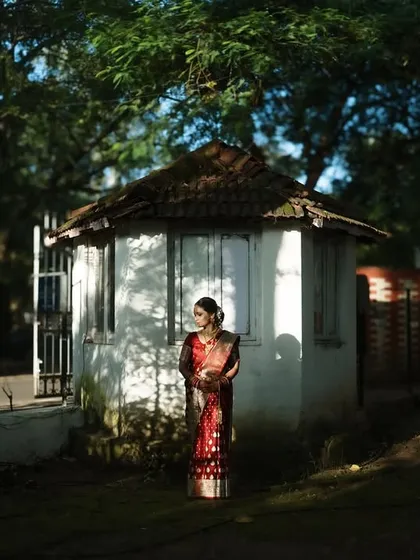 An environmental portrait of the bride in a rustic setting. The contrast between her vibrant saree and the simple hut creates a visually striking image.