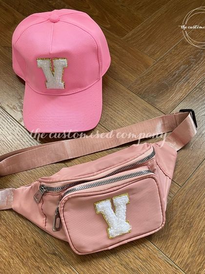 Pink essentials for a colorful summer holiday. This matching set includes a bright pink baseball cap and a multi-zipper fanny pack, both personalized with a sparkling initial patch.