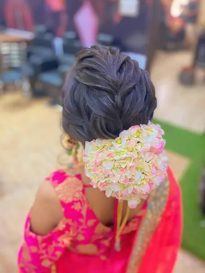 A braided updo finished with a large gajra of artificial flowers. This is a beautiful style for a traditional ceremony, combining a classic braid with a floral bun.