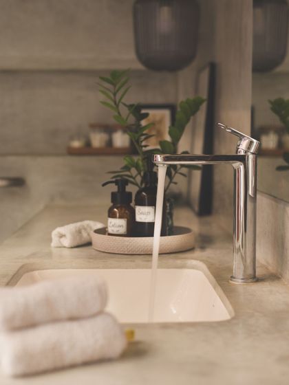A close-up of the cast-in-situ concrete washbasin. We believe in finding beauty in simple, honest materials, complemented here by thoughtfully chosen accessories and a touch of greenery.