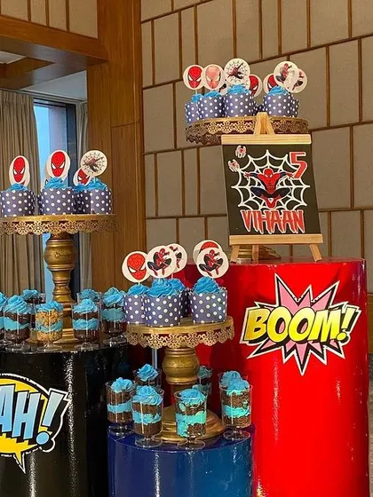 A detailed look at the Spider-Man themed treats, including cupcakes with character toppers, displayed on themed barrels with comic book sound effects like 'BOOM!' and 'YEAH!'.