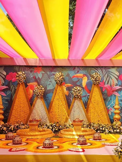 For this outdoor Haldi ceremony, I used a combination of bright pink and yellow fabric draping for the canopy. The backdrop features a custom tropical print, and the stage is decorated with marigold and tuberose floral structures.