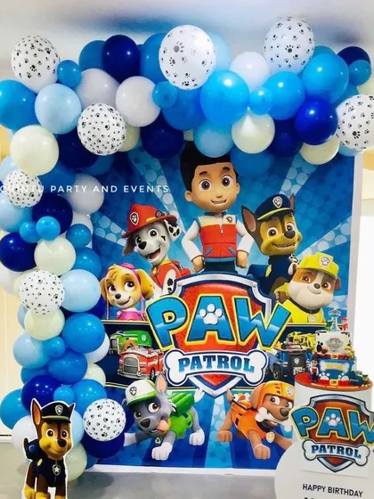 A fun Paw Patrol themed birthday party setup. This decoration features a character-filled backdrop, a blue and white balloon arch with paw print details, and cutouts of the heroic pups.
