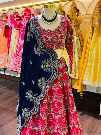 A vibrant red lehenga with a contrasting navy blue velvet dupatta. This mannequin showcases how we style traditional pieces with a modern, regal touch.