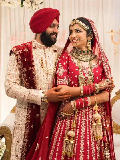 A beautiful portrait of a Sikh couple, showcasing the bride's vibrant red lehenga and the groom's traditional attire with a red turban.