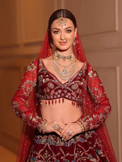 A smiling bride in her stunning red lehenga. The sheer dupatta adds a touch of softness to the opulent, heavily embroidered outfit.