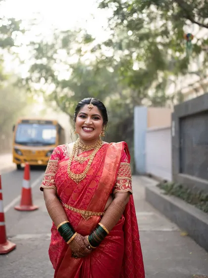 A happy street-side portrait of the bride, her red saree vibrant against the urban backdrop.