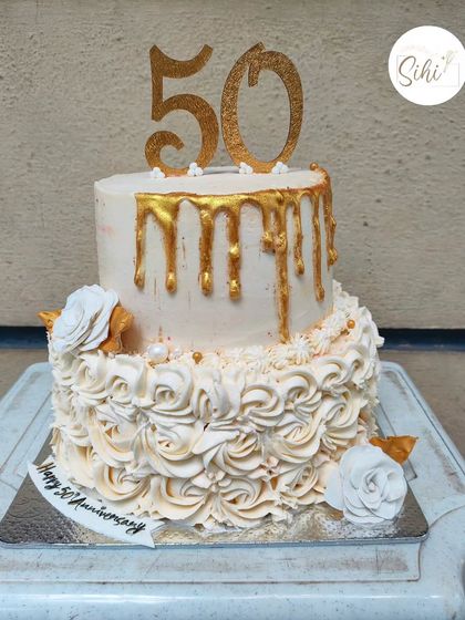 Celebrating a golden anniversary with a cake to match. This two-tiered design for a 50th anniversary features a cascade of buttercream rosettes on the bottom and a beautiful gold drip on top.
