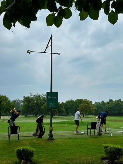 A view of the range through the leaves, showing golfers scattered across the practice area.